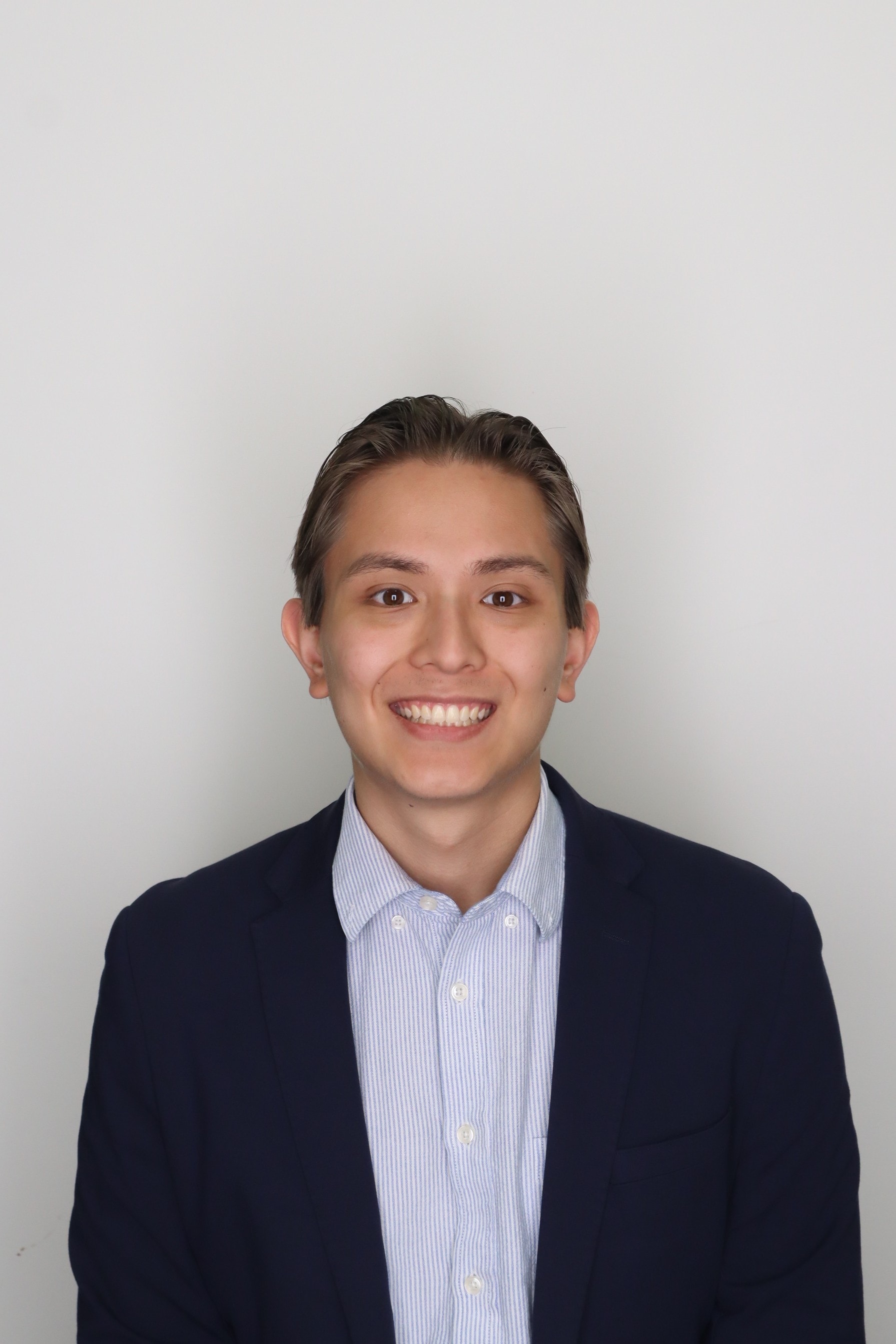 Ehsan smiling in a navy blazer and striped button-down shirt
