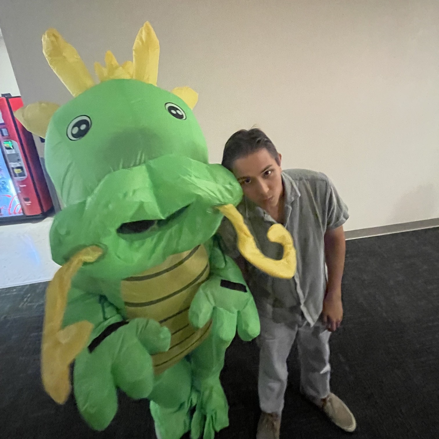 Ehsan leaning on a friend in an inflatable green dragon costume at Knight Hacks